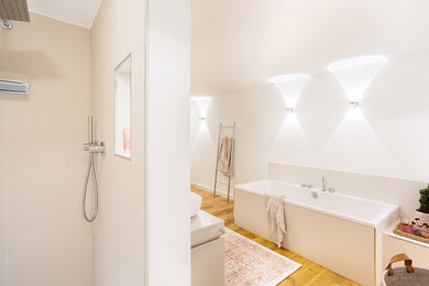 Geräumiges Modernes Badezimmer En Suite mit Einbaubadewanne, weißer Wandfarbe, braunem Holzboden, braunem Boden, flächenbündigen Schrankfronten, beigen Schränken, bodengleicher Dusche, Wandtoilette, beigen Fliesen, Mosaikfliesen, Aufsatzwaschbecken, Mineralwerkstoff-Waschtisch und beiger Waschtischplatte