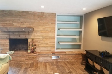 Example of a huge minimalist open concept porcelain tile and brown floor living room design in Oklahoma City with beige walls, a standard fireplace, a stone fireplace and a wall-mounted tv