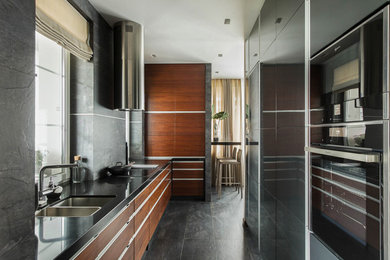 This is an example of a contemporary l-shaped kitchen in Moscow with an undermount sink, flat-panel cabinets, medium wood cabinets, grey splashback, black appliances, grey floor and black benchtop.
