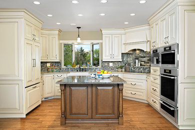 Example of a large classic u-shaped medium tone wood floor and brown floor eat-in kitchen design in Edmonton with a farmhouse sink, raised-panel cabinets, white cabinets, quartz countertops, multicolored backsplash, mosaic tile backsplash, stainless steel appliances, an island and multicolored countertops