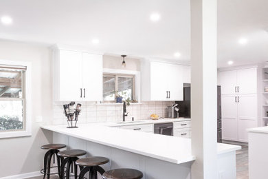 Example of a mid-sized classic u-shaped laminate floor open concept kitchen design in Dallas with an undermount sink, shaker cabinets, white cabinets, quartz countertops, beige backsplash, ceramic backsplash, stainless steel appliances, no island and white countertops