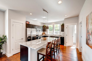 Medium tone wood floor and brown floor kitchen photo in Denver with an undermount sink, shaker cabinets, dark wood cabinets, granite countertops, stainless steel appliances and an island