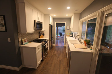 Eat-in kitchen - brown floor eat-in kitchen idea in Los Angeles with white cabinets, gray backsplash, stainless steel appliances and white countertops