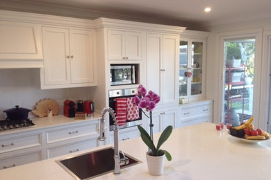 This is an example of a mid-sized country single-wall open plan kitchen in Central Coast with a drop-in sink, recessed-panel cabinets, white cabinets, marble benchtops, white splashback, ceramic splashback, stainless steel appliances, ceramic floors, with island, white floor and white benchtop.