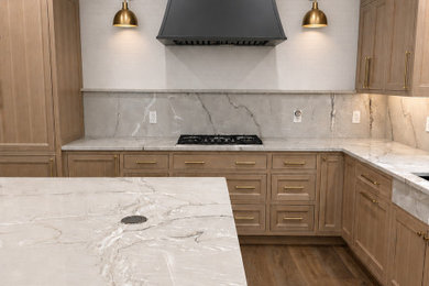 Inspiration for a mid-sized transitional u-shaped light wood floor kitchen remodel in Oklahoma City with an undermount sink, flat-panel cabinets, light wood cabinets, quartzite countertops, white backsplash, stainless steel appliances, an island and gray countertops