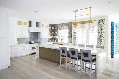 Photo of a beach style u-shaped kitchen in Orange County with beaded inset cabinets, white cabinets, beige splashback, white appliances, light hardwood floors, with island and beige floor.