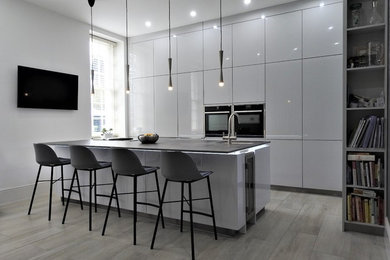 Design ideas for a medium sized modern l-shaped open plan kitchen in Kent with a submerged sink, flat-panel cabinets, white cabinets, black appliances, an island and blue worktops.