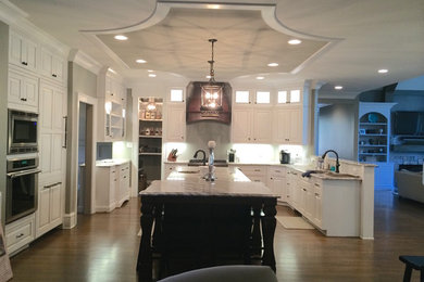 Example of a large transitional u-shaped dark wood floor open concept kitchen design in Raleigh with an undermount sink, raised-panel cabinets, white cabinets, quartz countertops, white backsplash, stainless steel appliances, an island and beige countertops