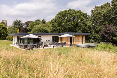 Photo of a large and brown contemporary detached house in West Midlands with wood cladding, a flat roof and board and batten cladding.