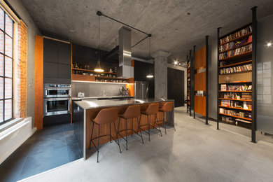 This is an example of a mid-sized industrial kitchen in Montreal with flat-panel cabinets, black cabinets, stainless steel benchtops, grey splashback, slate splashback, stainless steel appliances, slate floors, with island, grey floor and an undermount sink.