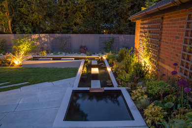 Photo of a medium sized contemporary back partial sun garden in Hertfordshire with a pond and natural stone paving.