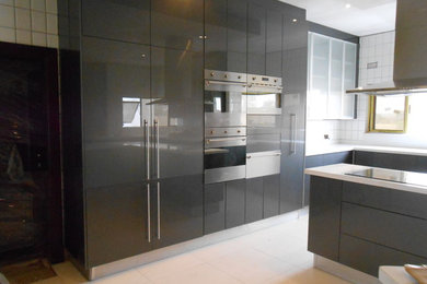 Example of a huge minimalist u-shaped porcelain tile eat-in kitchen design in Other with a drop-in sink, flat-panel cabinets, gray cabinets, granite countertops, white backsplash, porcelain backsplash, stainless steel appliances and an island
