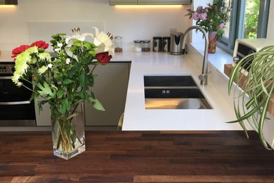 Medium sized contemporary u-shaped kitchen in Surrey with flat-panel cabinets, white cabinets, white splashback, a breakfast bar, brown floors and white worktops.