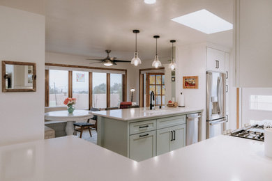 アルバカーキにある高級な中くらいなコンテンポラリースタイルのおしゃれなキッチン (シングルシンク、シェーカースタイル扉のキャビネット、緑のキャビネット、白いキッチンパネル、サブウェイタイルのキッチンパネル、シルバーの調理設備、淡色無垢フローリング、茶色い床、白いキッチンカウンター) の写真