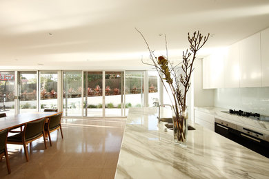 This is an example of a modern kitchen in Melbourne with marble benchtops, white splashback and marble floors.
