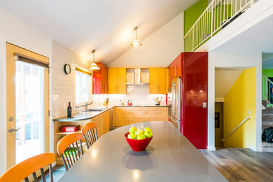 Example of a mid-sized trendy u-shaped medium tone wood floor and brown floor open concept kitchen design in Denver with a drop-in sink, flat-panel cabinets, red cabinets, quartz countertops, gray backsplash, ceramic backsplash, stainless steel appliances, an island and gray countertops
