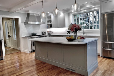 Inspiration for a large transitional l-shaped medium tone wood floor and exposed beam eat-in kitchen remodel in Philadelphia with white cabinets, marble countertops, white backsplash, stainless steel appliances, an island, white countertops, an undermount sink, recessed-panel cabinets and ceramic backsplash