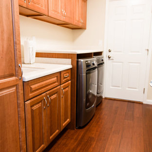 シアトルの大きいトラディショナルスタイルのおしゃれな家事室 (アンダーカウンターシンク、レイズドパネル扉のキャビネット、中間色木目調キャビネット、人工大理石カウンター、ベージュの壁、竹フローリング、左右配置の洗濯機・乾燥機、茶色い床) の写真