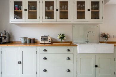 Design ideas for a medium sized traditional galley kitchen/diner in Sussex with a belfast sink, shaker cabinets, green cabinets, wood worktops, glass sheet splashback and no island.