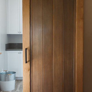 Inspiration for a large country l-shaped separated utility room in Boston with a submerged sink, shaker cabinets, white cabinets, composite countertops, grey walls, plywood flooring and a stacked washer and dryer.