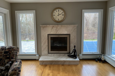 This is an example of a small traditional living room in New York with grey walls, a standard fireplace, a stone fireplace surround and brown floors.