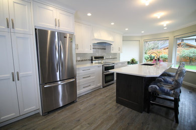 Example of a mid-sized transitional galley medium tone wood floor and brown floor kitchen design in Vancouver with an undermount sink, shaker cabinets, white cabinets, quartzite countertops, white backsplash, subway tile backsplash, stainless steel appliances and an island