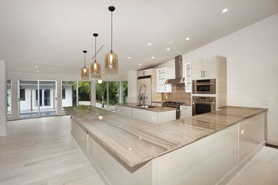 This is an example of a large contemporary u-shaped open plan kitchen in Miami with an undermount sink, flat-panel cabinets, white cabinets, marble benchtops, beige splashback, marble splashback, stainless steel appliances and with island.
