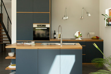 Modelo de cocina contemporánea de tamaño medio abierta con armarios con paneles lisos, puertas de armario azules, encimera de madera, suelo de cemento, una isla, suelo gris y encimeras marrones