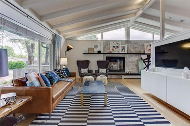 Inspiration for a mid-sized 1960s open concept light wood floor and beige floor living room remodel in Denver with white walls, a standard fireplace, a stone fireplace and a wall-mounted tv