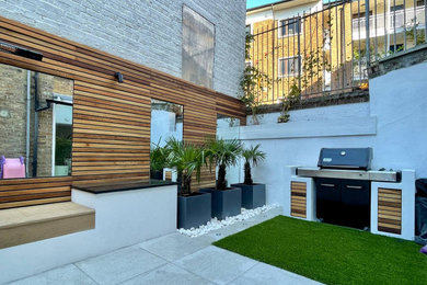 This is an example of an expansive modern courtyard patio in London with a bbq area.