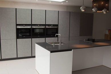 Inspiration for a large contemporary single-wall open plan kitchen in West Midlands with a built-in sink, flat-panel cabinets, white cabinets, quartz worktops, black appliances, porcelain flooring, an island and grey floors.