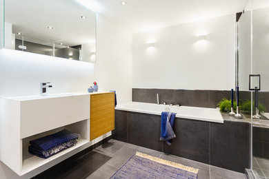 Mittelgroßes Modernes Duschbad mit flächenbündigen Schrankfronten, hellen Holzschränken, Einbaubadewanne, bodengleicher Dusche, Wandtoilette, schwarzen Fliesen, weißer Wandfarbe, Wandwaschbecken, Mineralwerkstoff-Waschtisch und schwarzem Boden in Köln