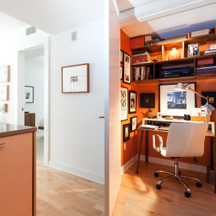 Modern inredning av ett litet arbetsrum, med orange väggar, ljust trägolv och ett fristående skrivbord