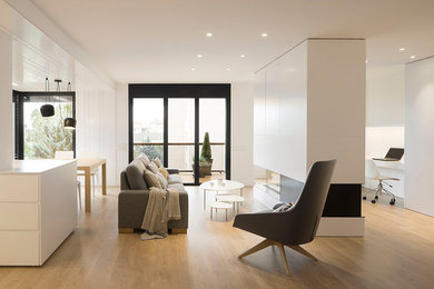 Photo of a mid-sized scandinavian open concept living room in Barcelona with white walls, medium hardwood floors, a two-sided fireplace, a wood fireplace surround, brown floor and a concealed tv.
