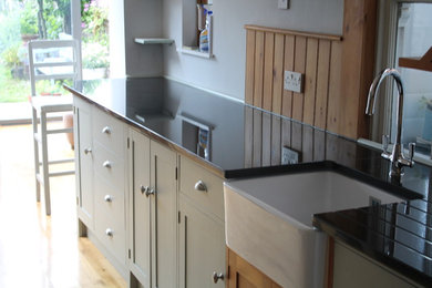 This is an example of a traditional kitchen/diner in Hampshire with shaker cabinets, grey cabinets, granite worktops, black appliances, no island, a belfast sink and light hardwood flooring.