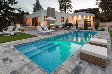 Modelo de piscina alargada contemporánea grande rectangular en patio trasero con adoquines de hormigón