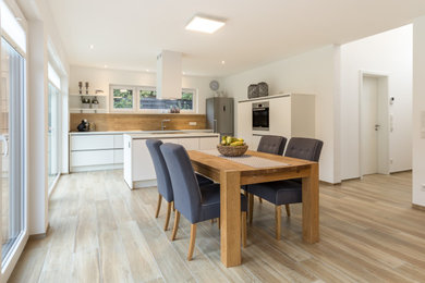 Offene, Zweizeilige, Geräumige Moderne Küche mit integriertem Waschbecken, weißen Schränken, Rückwand aus Holz, Küchengeräten aus Edelstahl, hellem Holzboden, Kücheninsel und weißer Arbeitsplatte in Sonstige