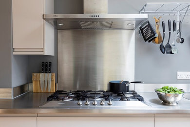 Photo of a contemporary kitchen/diner in London with flat-panel cabinets, medium wood cabinets, stainless steel worktops and stainless steel appliances.