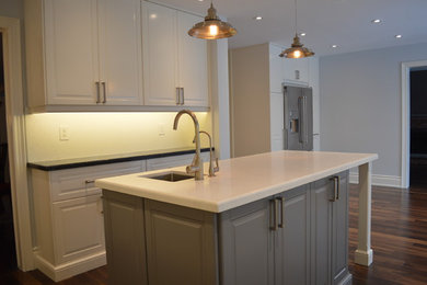 This is an example of a large traditional u-shaped eat-in kitchen in Toronto with a single-bowl sink, raised-panel cabinets, white cabinets, quartz benchtops, white splashback, stainless steel appliances, medium hardwood floors and with island.