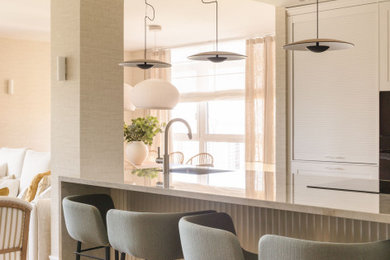 Diseño de cocina beige y blanca clásica renovada grande abierta con fregadero bajoencimera, armarios con paneles lisos, puertas de armario blancas, encimera de cuarzo compacto, electrodomésticos negros, suelo laminado, península, suelo beige, encimeras beige y barras de cocina