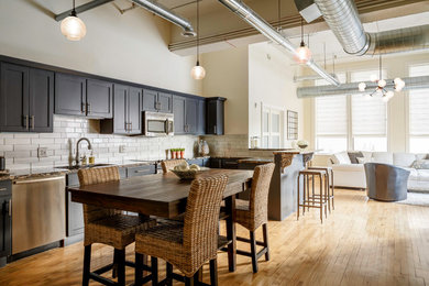Example of a transitional u-shaped medium tone wood floor and brown floor open concept kitchen design in Grand Rapids with shaker cabinets, black cabinets, white backsplash, subway tile backsplash, stainless steel appliances and no island