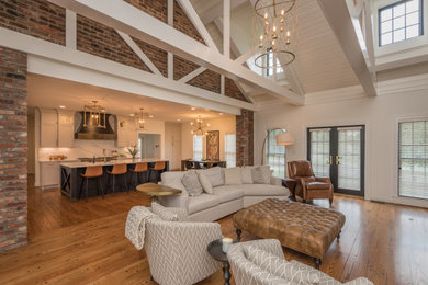 Inspiration for a large traditional open concept family room in Louisville with white walls, light hardwood floors, a standard fireplace, a brick fireplace surround, no tv, brown floor and exposed beam.