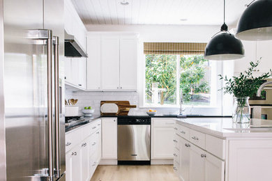 Design ideas for a mid-sized country l-shaped kitchen in Seattle with an undermount sink, shaker cabinets, white cabinets, quartz benchtops, white splashback, ceramic splashback, stainless steel appliances, light hardwood floors, with island, beige floor and white benchtop.