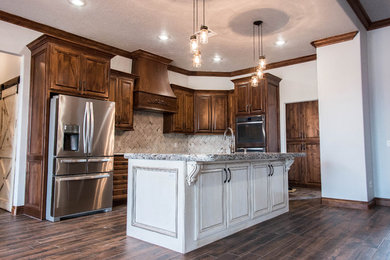 Mid-sized mountain style l-shaped dark wood floor open concept kitchen photo in Oklahoma City with an undermount sink, raised-panel cabinets, dark wood cabinets, granite countertops, beige backsplash, stone tile backsplash, stainless steel appliances and an island