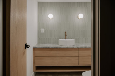 Example of a mid-sized danish green tile and ceramic tile marble floor and gray floor powder room design in Toronto with flat-panel cabinets, light wood cabinets, a two-piece toilet, white walls, a vessel sink, quartz countertops, gray countertops and a floating vanity
