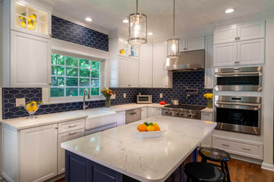 Inspiration for a large transitional l-shaped medium tone wood floor and brown floor open concept kitchen remodel in Other with a farmhouse sink, raised-panel cabinets, white cabinets, quartz countertops, blue backsplash, porcelain backsplash, stainless steel appliances, an island and white countertops