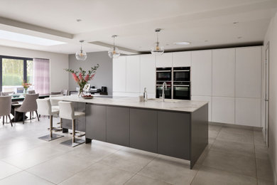 Design ideas for a large contemporary grey and white open plan kitchen in Buckinghamshire with an integrated sink, grey cabinets, laminate countertops, black appliances, ceramic flooring, an island, grey floors, white worktops and a feature wall.