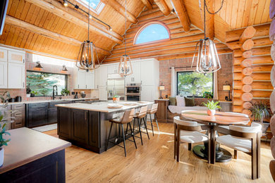 Huge mountain style u-shaped exposed beam open concept kitchen photo with a farmhouse sink, shaker cabinets, dark wood cabinets, stainless steel appliances and an island