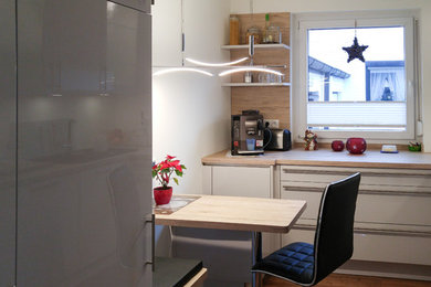 Inspiration for a small contemporary l-shaped separate kitchen in Hamburg with black appliances, no island, a drop-in sink, flat-panel cabinets, white cabinets, wood benchtops and brown splashback.