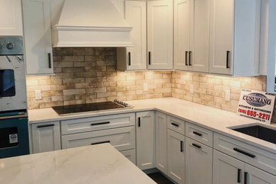 Eat-in kitchen - mid-sized transitional l-shaped brown floor and porcelain tile eat-in kitchen idea in New York with an undermount sink, recessed-panel cabinets, white cabinets, quartz countertops, beige backsplash, subway tile backsplash, stainless steel appliances, an island and white countertops